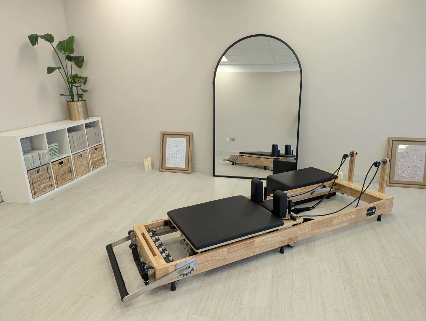 Foldable Gym Gear reformer with oak frame, shown in a studio setting, featuring padded carriage and adjustable resistance settings.